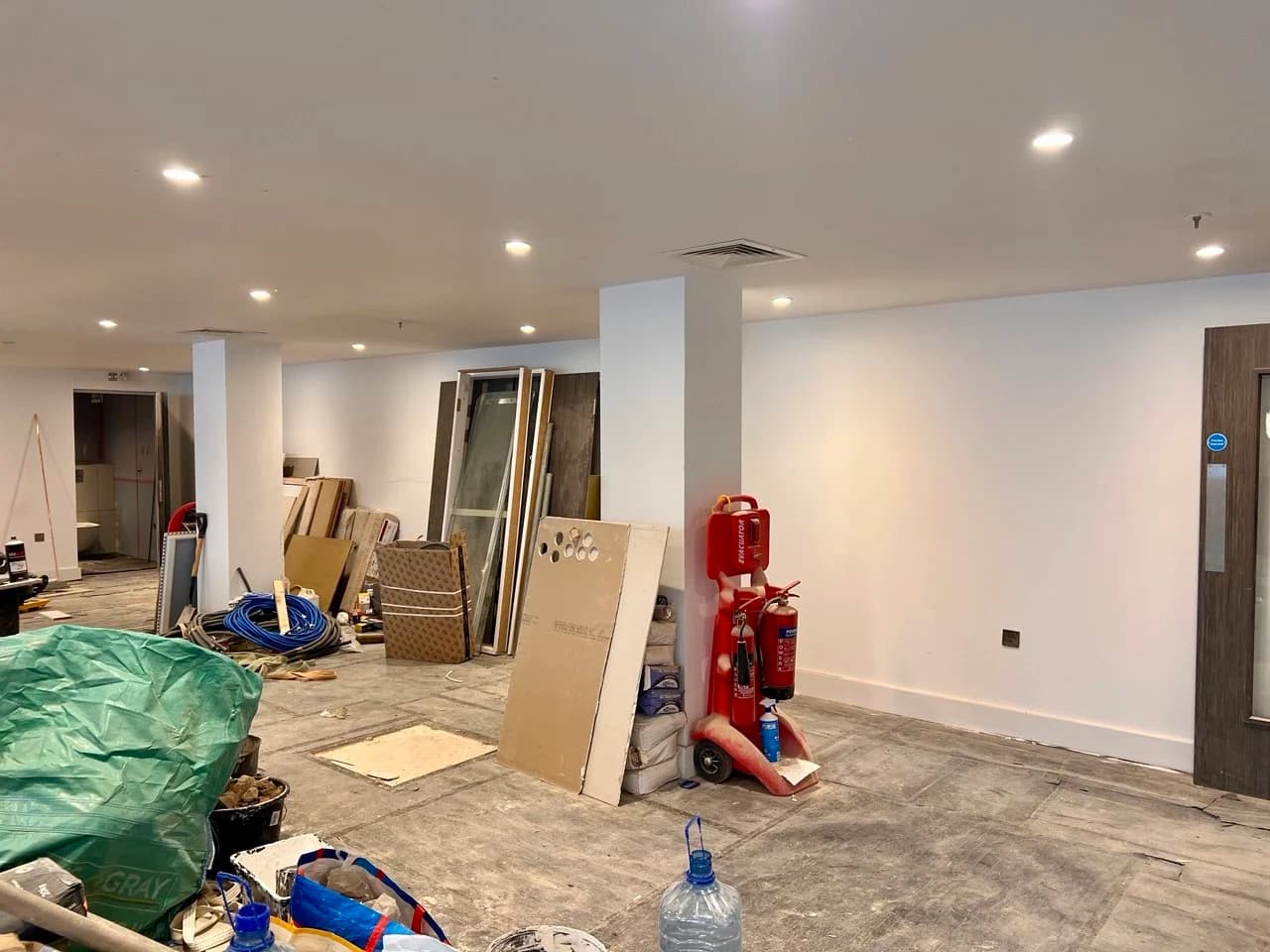 Restaurant dining room mid-renovation with bare walls, an unfinished floor and building materials stacked around