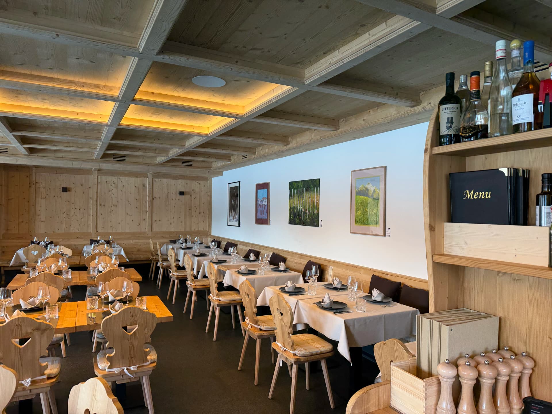 Restaurant dining room with a timber ceiling, set tables and framed artworks along a white wall